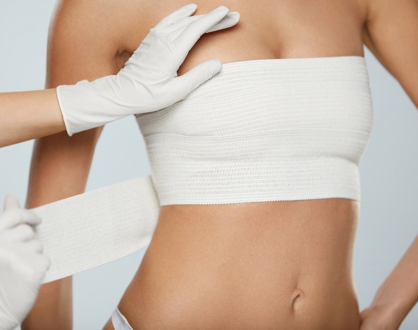 Cirurgião Plástico em Curitiba: A imagem mostra um profissional médico enfaixando as mamas de uma paciente após um procedimento cirúrgico.